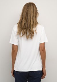 T-shirt blanc à manches courtes en coton avec une coupe décontractée, présentant un col rond et une texture lisse. Design classique sans embellissements.
