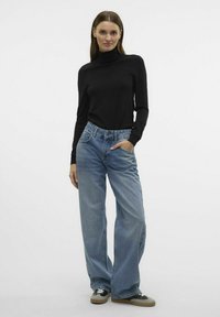 Črni pulover s turtleneck ovratnikom in svetlo modri široki hlačami. Hlače imajo visok pas in nekoliko poškodovan videz, obute pa so v črne in bež superge.