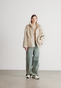 Beežikarva kohev jakk krae ja kahe taskuga, kantud helel mustrilisel särgil. Rohelised laia säärega püksid ja valged tossud täiustavad komplekti.