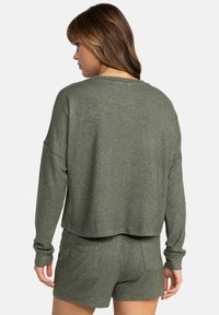Olive green cropped sweatshirt with long sleeves, relaxed fit, and a soft texture. Paired with matching shorts featuring side pockets.