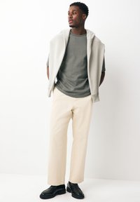 Lichtgrijze sweatshirt over een gestructureerd donkergroen shirt, gecombineerd met lichtbeige broek en zwarte loafers. Eenvoudig, modern ontwerp.