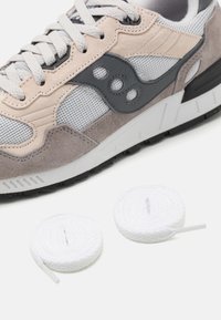 Tenisice s gornjim dijelom od sive i bež suede i mrežastog materijala, s crnim detaljima, bijelim vezicama i teksturiranim gumiranim potplatom. Uključuju dodatne bijele vezice.
