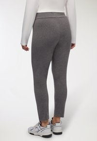 Leggings grigi realizzati in materiale morbido e elasticizzato con vita alta, che mostrano una vestibilità aderente fino alle caviglie, abbinati a sneakers bianche.