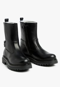 Zwarte leren enkellaarsjes met een zijrits, ronde neus en een profielzool. Voorzien van stiksel details en een kleine gesp aan de zijkant.