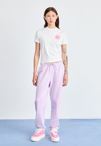 Hvit bomulls T-skjorte med rosa grafikk på brystet, kombinert med lavendel joggebukser og rosa platåsko med hvite snørebånd.