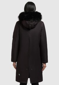 Sort parka med en faux fur hætte, lange ærmer og to trykknapper i kanten. Har en glat, shiny tekstur og en lomme ved siden af ærmet.