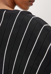 Czarny top z tkaniny z pionowymi teksturowanymi paskami, podkreślonymi cienkimi białymi liniami. Design ma okrągły dekolt i miękką teksturę.