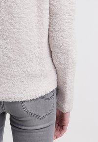 Hellgrauer, flauschiger Pullover mit weicher Textur, ausgestattet mit einem Rundhalsausschnitt und einer leicht lockeren Passform, kombiniert mit grauen Denim-Jeans.