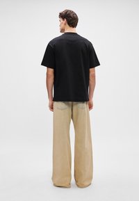 Μαύρο βαμβακερό T-shirt με κοντά μανίκια, σε συνδυασμό με φαρδιά μπεζ παντελόνια που διαθέτουν διακριτική ραφή και σχέδιο με πέντε τσέπες.