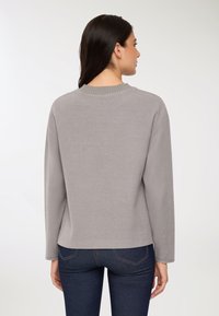 Szary pulower z ribbowanym kołnierzem i długimi rękawami. Miękka tkanina, luźny krój i prosty dół. Noszony z ciemnoniebieskimi dżinsami.