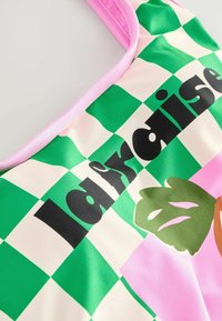 Grön och rosa rutigt tygkasse med svart text "la française" och blommiga grafik, med en rosa rem och slät textur.