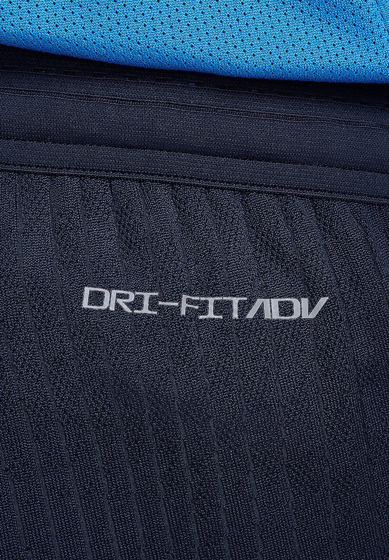 Pantalón corto Navy Dri-FIT ADV con un tejido texturizado y un logo reflectante plateado. La parte superior es de color azul claro con un patrón de malla.
