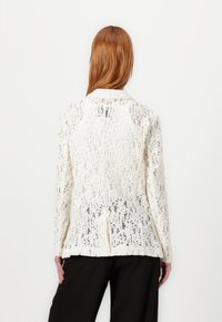 Lace jacket in off-white with a textured pattern. Features a collar, long sleeves, and a tailored fit. Back view displayed.