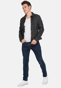 Svart läderjacka med dragkedja på framsidan och sidofickor, i kombination med en vit t-shirt och blå jeans, kompletterad med vita sneakers.