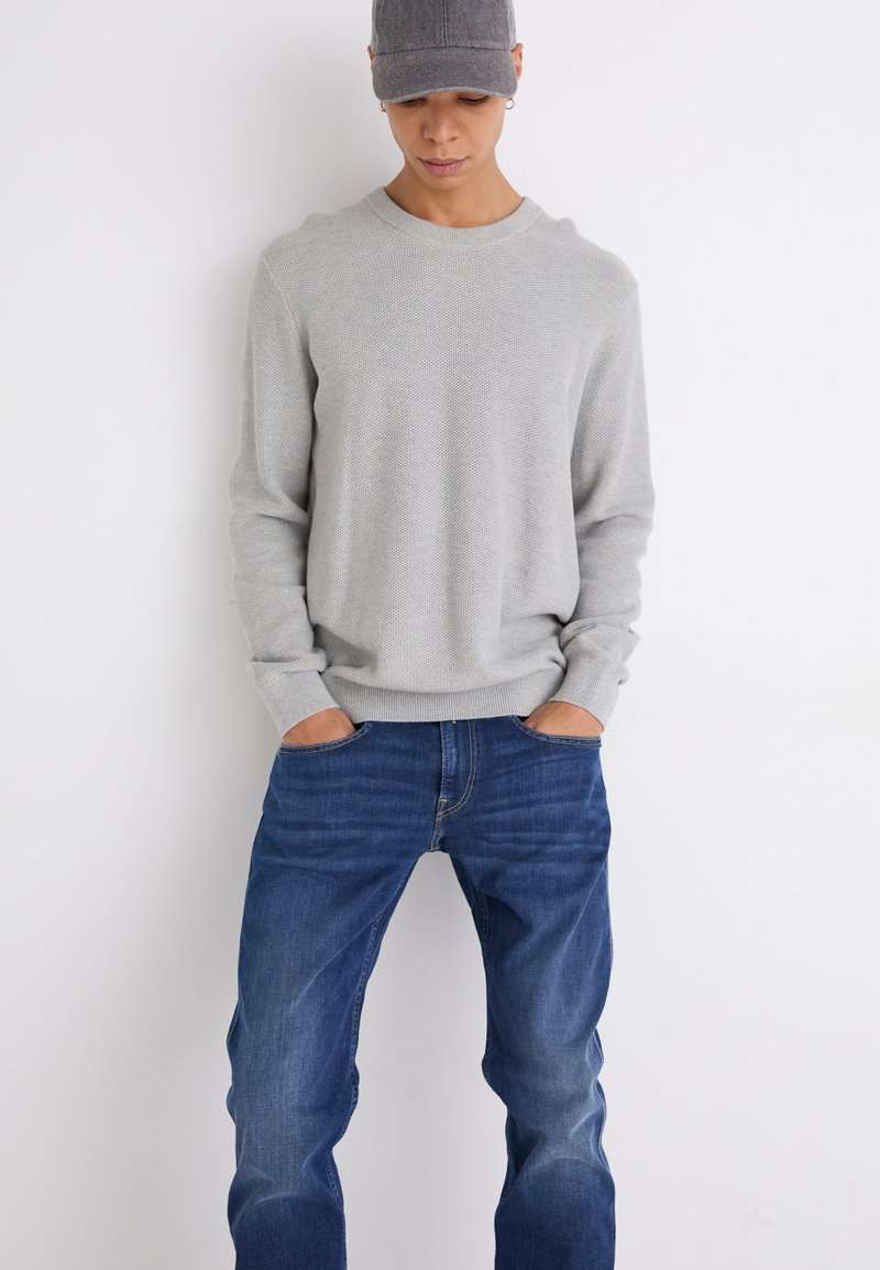 Lichtgrijze gebreide trui met ronde halslijn en ribgebreide manchetten, gecombineerd met blauwe denim jeans met een klassieke pasvorm en vijf-pocket ontwerp.