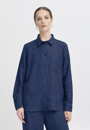 Navy blue button-up shirt made of textured fabric, featuring a chest pocket and long sleeves with a relaxed fit. Subtle white streaks throughout.