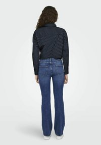 Blårandig skjorta med krage, matchad med utsvängda blå jeans. Jeansen har bakfickor och har en avslutad fåll.