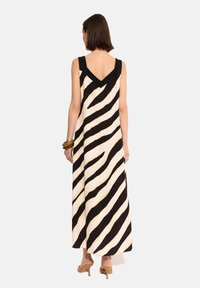 Maxi sukienka w kremowym kolorze z wyraźnymi czarnymi ukośnymi paskami. Posiada szerokie ramiączka, dekolt w kształcie litery V z tyłu i gładki materiał. Stylizowana z brązowymi obcasami.
