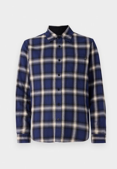 Sinine ja valge ruuduline pikkade varrukatega särk, millel on nööpidega esiosa, krae ning mustad aktsendid mansettidel ja kaeluses. Omab tavalisi nööpe.