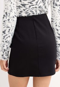 Minifalda negra con una textura suave y un dobladillo limpio, combinada con un suéter blanco de lana suave que presenta acentos de estampado de leopardo negro.