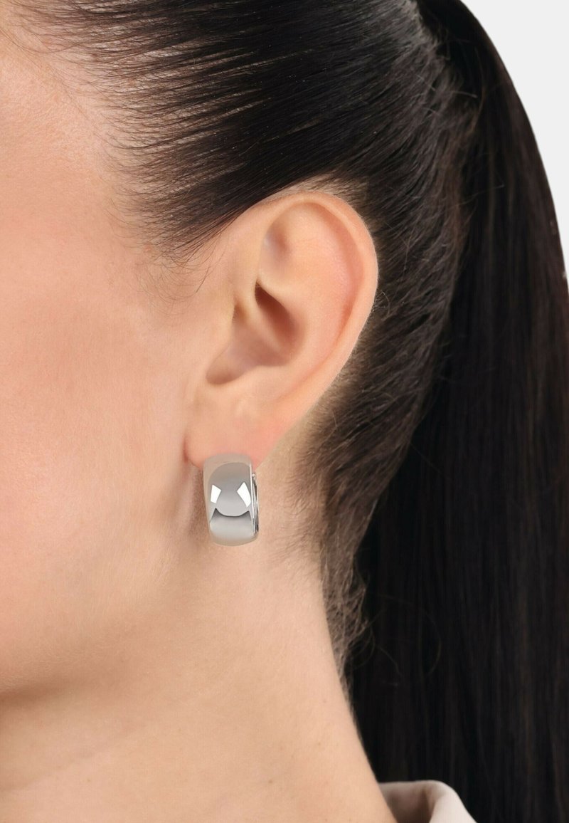 Silver hoopearring med en slät, polerad yta. Har en rundad form och en subtil geometrisk design. Bärs i örat.