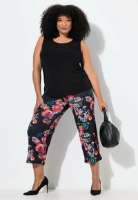 Zwarte mouwloze top gecombineerd met zwarte cropped broek met een kleurrijk bloemenpatroon. Model houdt een zwarte handtas vast en draagt zwarte hakken.