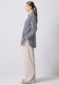 Camicia a righe blu navy e bianca, con maniche lunghe e orlo curvo. Abbinata a pantaloni a gamba larga color crema e scarpe chiare.