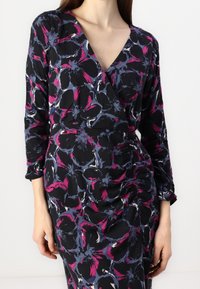 Black wrap dress with long sleeves, featuring a floral pattern in pink, blue, and white. Gathered detail adds texture to the side.