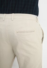 Beige bomullbyxor med bakficka och bälteshällor, med en jämn textur och en skräddarsydd passform.