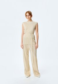 Lys guld, ærmeløs top med en plisseret tekstur og en bælte i taljen parret med vidde ben, high-waisted bukser i et lignende design.