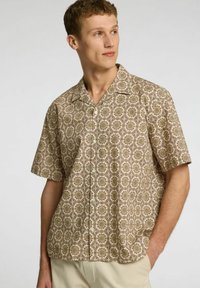 Camicia a maniche corte, di colore beige, con un motivo intrecciato di fiori in toni di marrone e oro, con chiusura a bottoni e un fit rilassato.