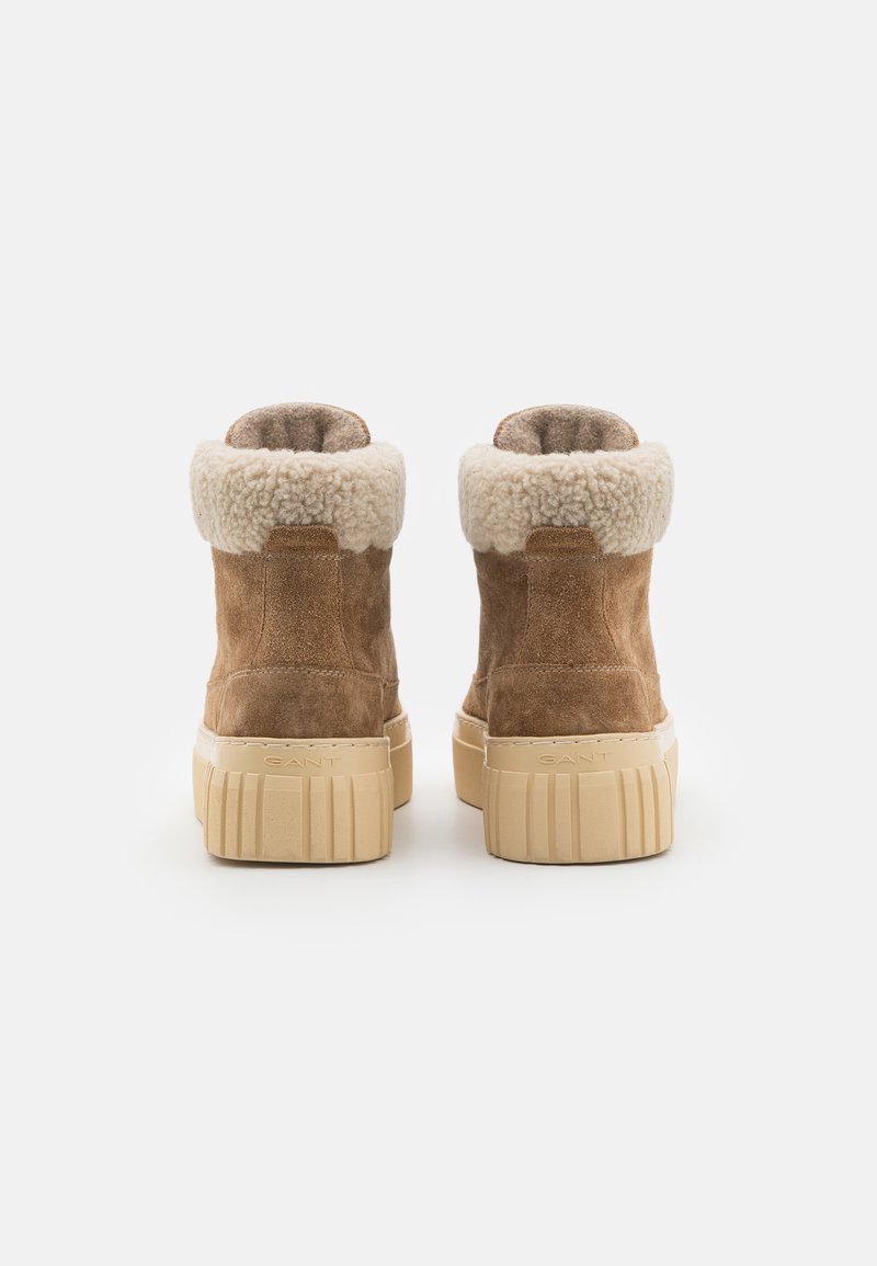 Bottines en daim marron avec un col en fausse fourrure crème et une épaisse semelle en caoutchouc beige, présentant un motif de grip texturé à la base.