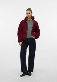 Burgundy puffers jakke med høj krave, lynlås lukning, parret med en grå kabelstrik sweater og højtaljede mørke denim jeans. Sorte ankelstøvler.