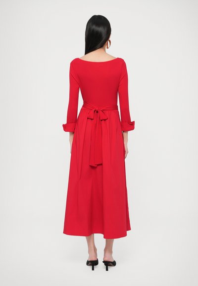 Piros, térdig érő ruha hosszú ujjakkal és megkötős hátrésszel. Simább anyag természetes eséssel. Kerek nyakkivágás és mandzsettás ujjú.