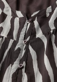 Blusa a righe bianco e nere con tessuto testurizzato, dotata di bottoni lungo la parte anteriore e un colletto rotondo. Dettaglio del motivo notevole.