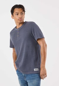Maglietta henley a maniche corte di colore blu navy, realizzata in tessuto strutturato, con tre bottoni in legno e una targhetta con logo all'orlo.