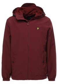 Bordowa kurtka z zamkiem z przodu, elastycznymi mankietami i kapturem. Charakteryzuje się wyraźnym żółtym logo na piersi, wykonana z gładkiego, wodoodpornego materiału.