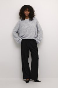 Grijze, oversized trui met een zachte textuur, gecombineerd met zwarte, op maat gemaakte, wijd uitlopende broeken. Zwarte pointy hakken maken de outfit compleet.