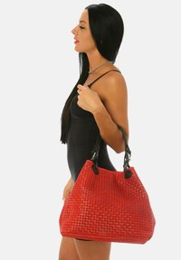 Röd vävd handväska med en texturerad yta och två svarta läderremmar fästa med silverfärgad hårdvara, med en rymlig form.
