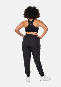 Schwarzer Sport-BH und taillierte Jogginghosen aus dehnbarem Material. Der BH hat ein Racerback-Design; die Jogginghosen verfügen über elastische Bündchen und Taschen.