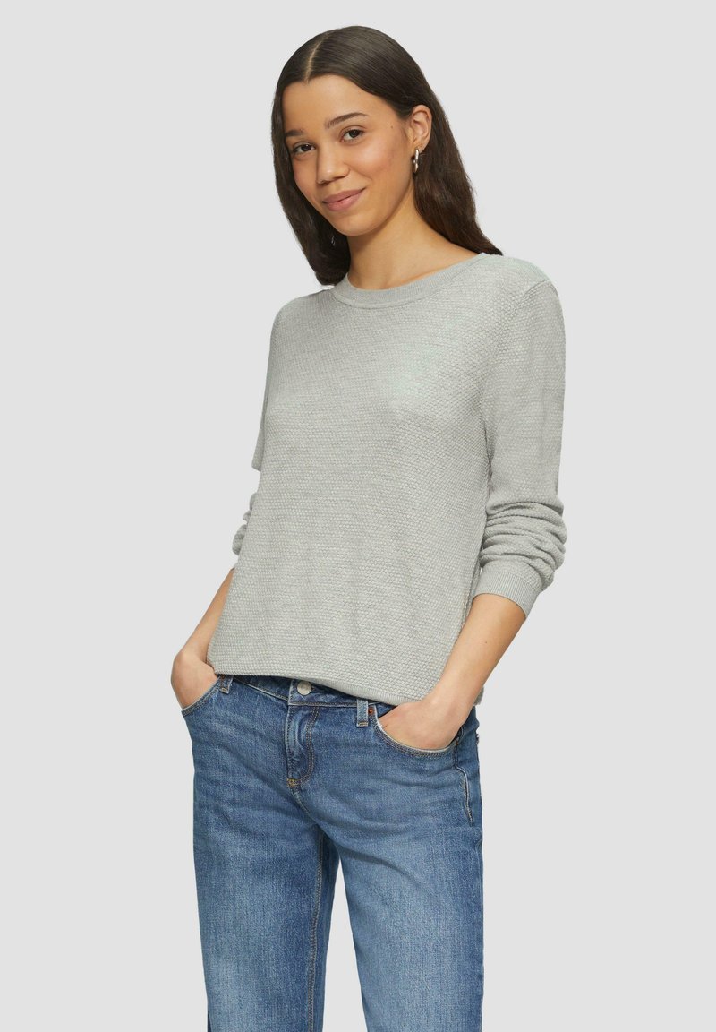 Hellgrauer strukturierter Pullover mit Rundhalsausschnitt und langen Ärmeln, kombiniert mit blauen Jeans. Der Stoff wirkt weich und lässig.