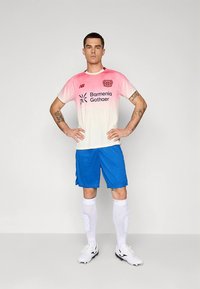 Focimez: rózsaszín-fehér átmenetes mez logóval, kék nadrággal, fehér térdmagasságú zoknival és fekete stoplis cipővel.