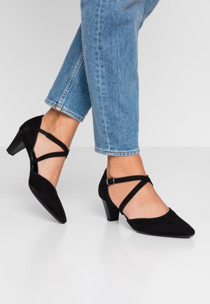 Schwarze Wildlederabsätze mit spitzem Zehenbereich und einem Blockabsatz mittlerer Höhe. Verfügt über überkreuzte Riemen mit einer Schnalle. Getragen mit cropped blauen Jeans.