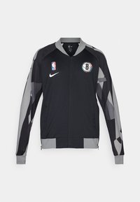 Black athletic jacket with gray accents, featuring a zip front, NBA logo, and Brooklyn Nets emblem, made from lightweight, textured fabric.