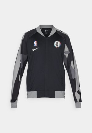 Black athletic jacket with gray accents, featuring a zip front, NBA logo, and Brooklyn Nets emblem, made from lightweight, textured fabric.