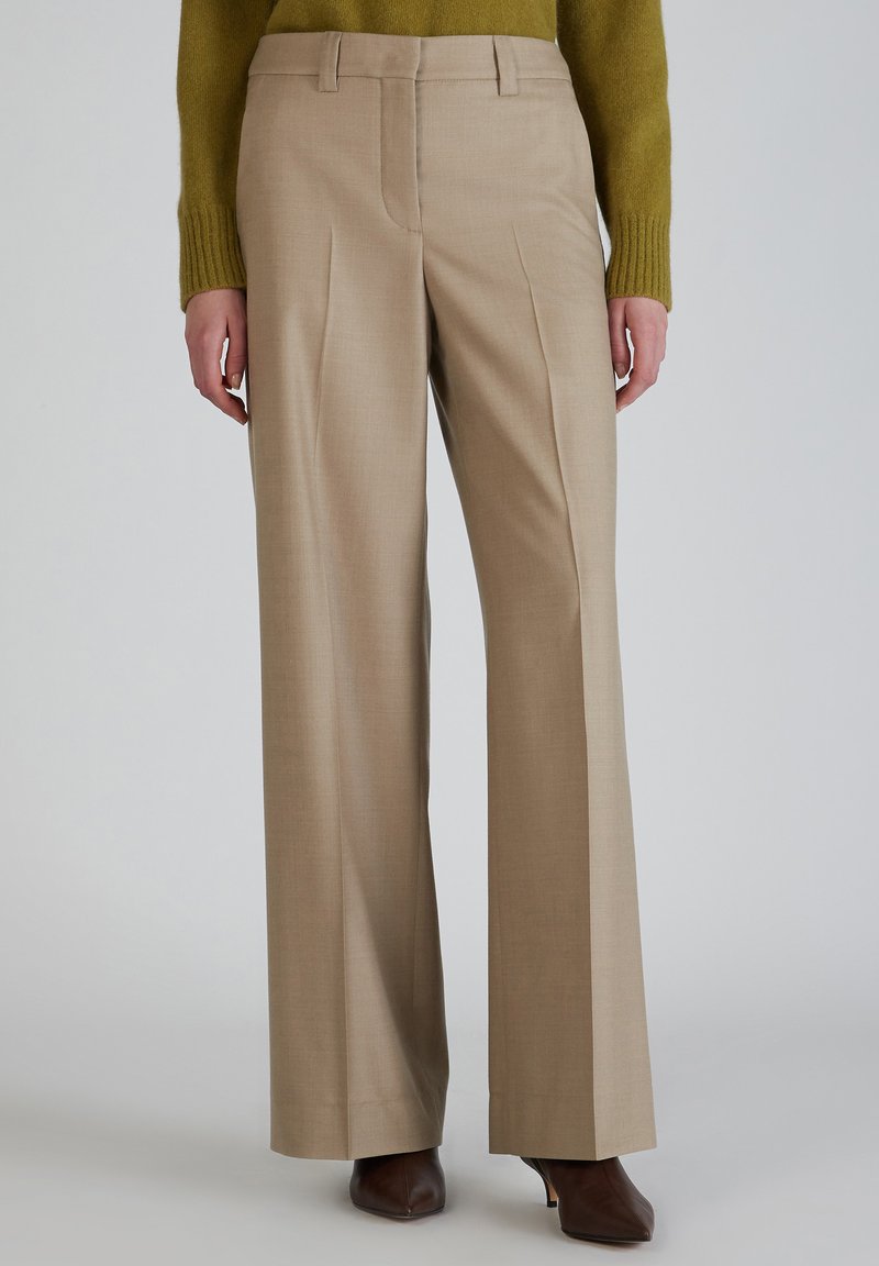 Beige wijde pijpenbroek met een gladde textuur, voorzien van voorplooien, een strakke tailleband en zijzakken. Gekoesterd met een groene trui.
