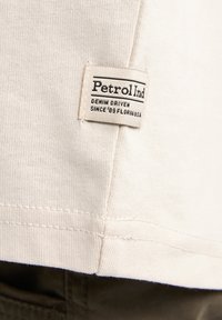 Beige katoenen shirt met een gestructureerd oppervlak; heeft een gestikte zoom. Het label leest "PetrolInd" met de tekst "DENIM DRIVEN SINCE '89 FLORIDA U.S.A."