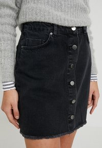 Svart denimkjol med fransad nederkant, med knäppning fram och sidofickor. Bärs med en ljusgrå stickad tröja.