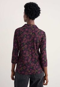 Dreiviertelarmhemd in Schwarz mit floralen Mustern in Lila-, Grün- und Rosatönen; Kragenverzierung und weicher Textur.