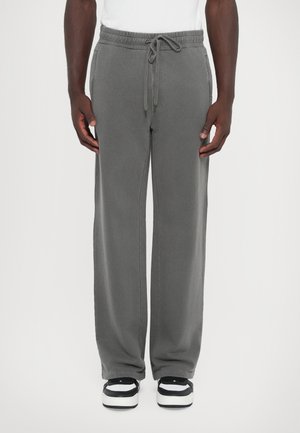 Graue Sweatpants mit einem Kordelzugbund, Seitentaschen und einer lockeren Passform, kombiniert mit schwarz-weißen Sneakern. Glatte Textur.